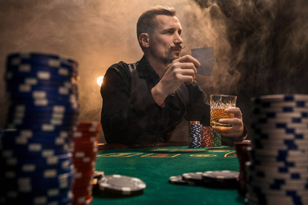 Handsome bearded man drinking whisky while playing poker - Photo, Image