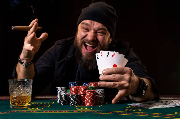 Γενειοφόρος άνδρας πίνει ουίσκι και καπνίζοντας ένα πούρο ενώ παίζοντας πόκερ - Φωτογραφία, εικόνα