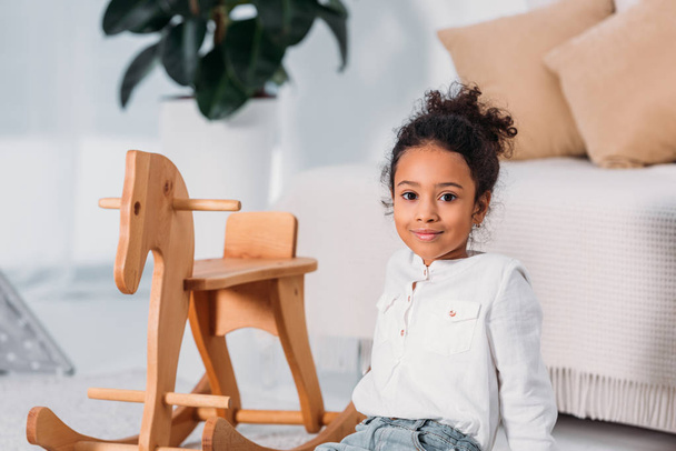 adorable african american kid sitting on floor near rocking horse - Photo, Image