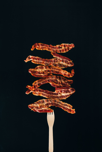 close up view of pieces of bacon on fork isolated on black - Photo, Image