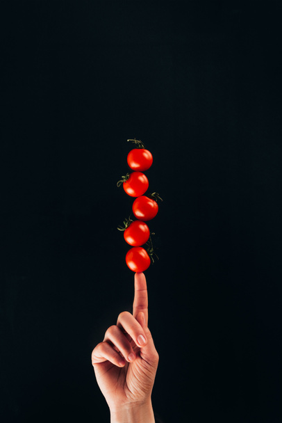 bijgesneden schot van vrouw met cherry tomaten op vinger geïsoleerd op zwart - Foto, afbeelding