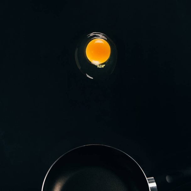 close up view of raw egg yolk falling on frying pan isolated on black - Fotoğraf, Görsel