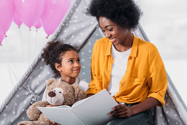 happy african american mother and daughter reading book together at home - Photo, image