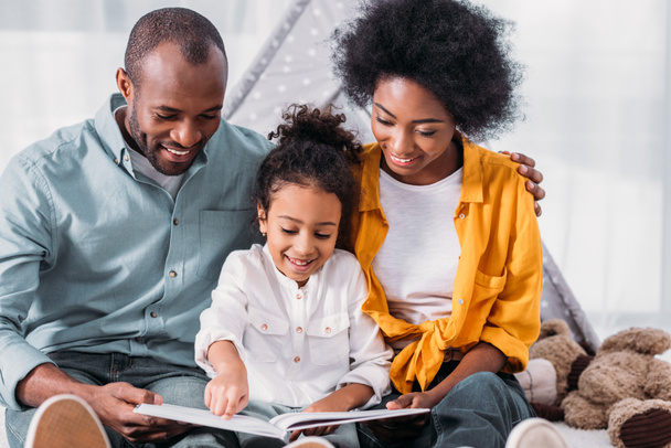 heureuse fille afro-américaine lecture pour les parents à la maison
 - Photo, image