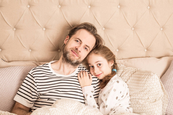 Father and daughter in pyjamas hugging in a bed - Fotó, kép