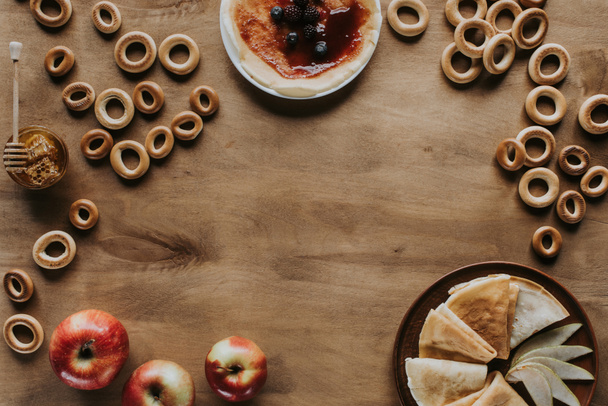 вид зверху смачні млинці з яблуками, ягодами, медом і бубликами на дерев'яному столі
 - Фото, зображення