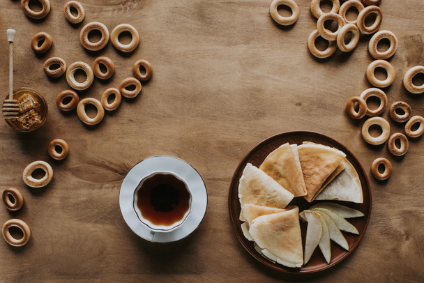 top view of tasty homemade pancakes with cup of tea, bagels and honey on wooden table - Fotoğraf, Görsel