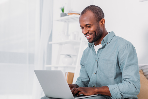 happy african american man using laptop on sofa at home - Foto, Imagen