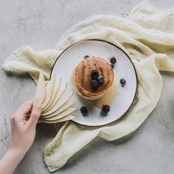 top view of person holding sliced pear above tasty homemade pancakes with berries and honey  - Foto, Imagem