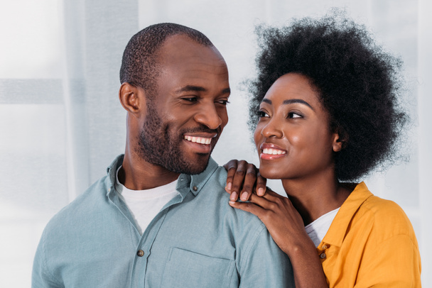 smiling african american couple hugging and looking at each other at home - Photo, image