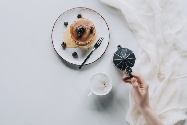 top view of person holding coffee maker while eating pancakes with berries for breakfast - Foto, afbeelding