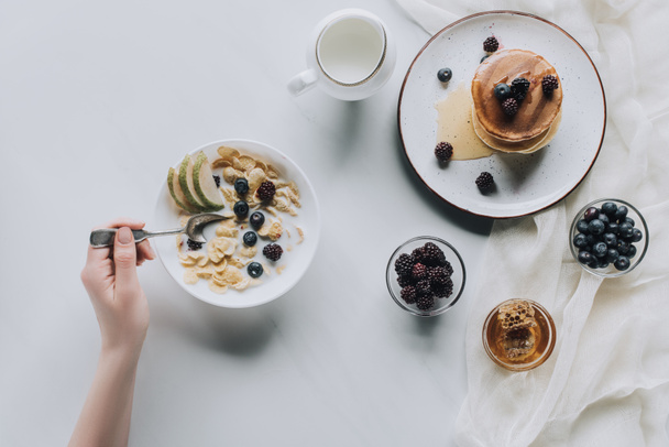 cropped shot of person eating fresh healthy breakfast with muesli and pancakes - Zdjęcie, obraz