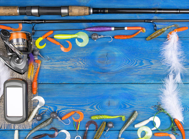 Fishing tackle - fishing spinning, fishing line, hooks, navigator and reel on blue wooden background - Foto, afbeelding