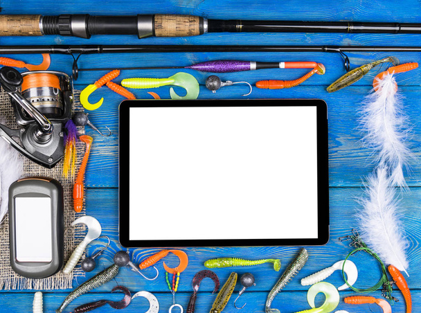 Fishing rod, tackles and fishing baits, reel on wooden board background with tablet computer isolated white screen, empty space for text - Photo, Image