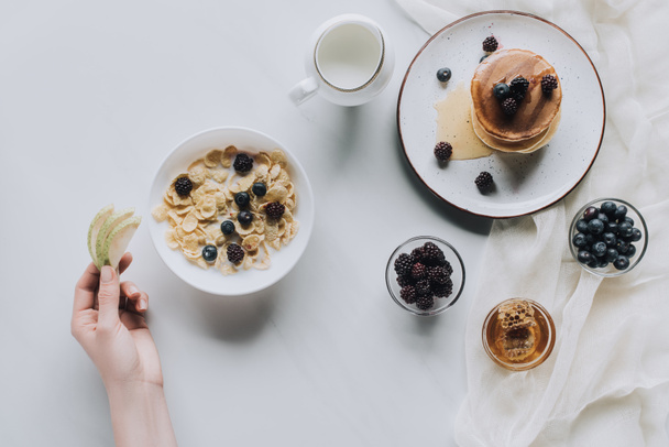 cropped shot of person eating healthy muesli and pancakes with fruits for breakfast on grey - Foto, Imagem