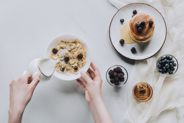 vista superior de la persona que vierte leche en un tazón con muesli durante el desayuno
 - Foto, Imagen