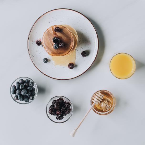 top view of fresh tasty pancakes with honey, berries and juice on grey  - Zdjęcie, obraz