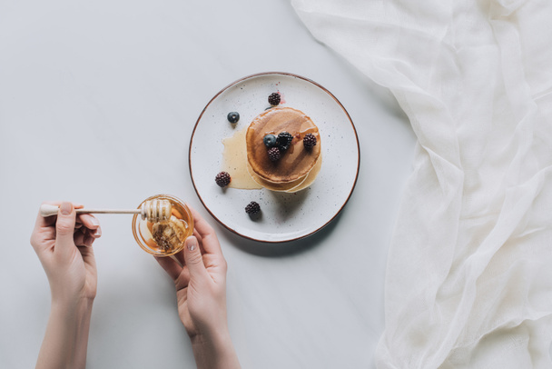 cropped shot of person eating delicious homemade pancakes with berries and honey on grey - Foto, afbeelding