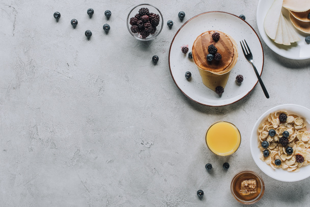 top view of delicious homemade breakfast with pancakes, fruits, honey and muesli on grey     - Foto, imagen