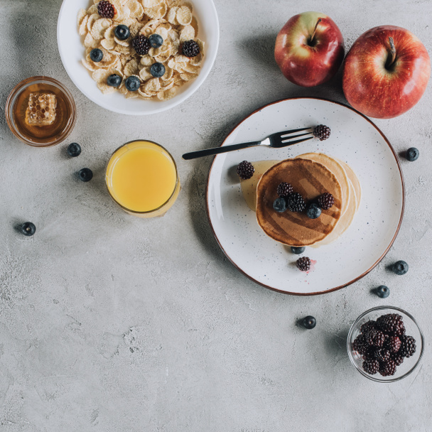 bovenaanzicht van zoete gastronomisch ontbijt met pannenkoeken, fruit, honing en muesli op grijs    - Foto, afbeelding