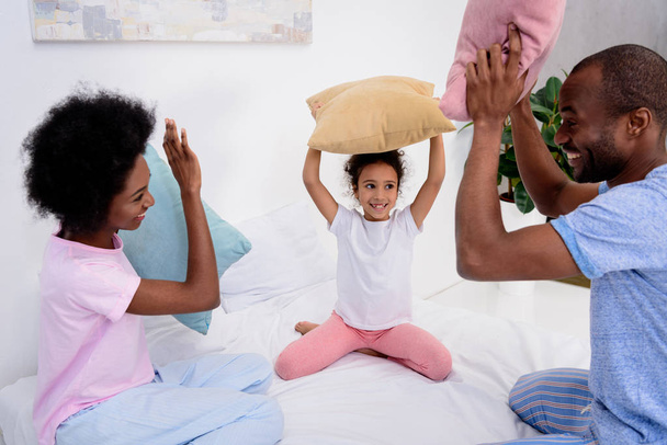african american parents and daughter having fun with pillows at home - Φωτογραφία, εικόνα