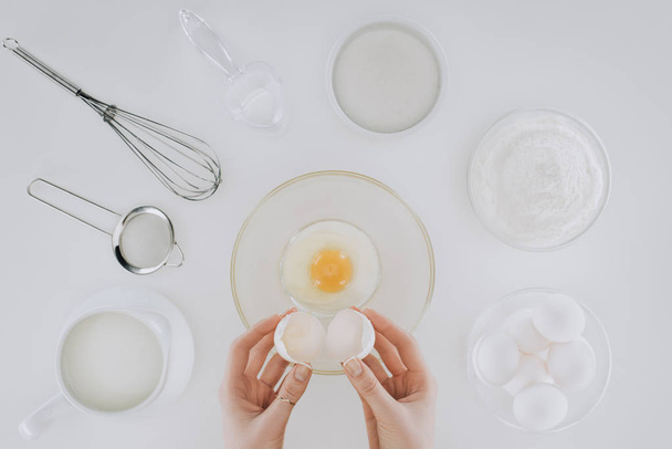 cropped shot of person holding eggshell while cooking pancakes isolated on grey - Foto, imagen