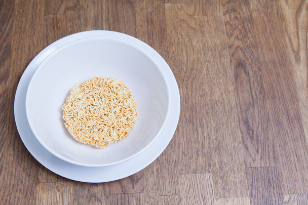 Fideos instantáneos sin cocer en tazón blanco y plato en mesa de madera
 - Foto, imagen