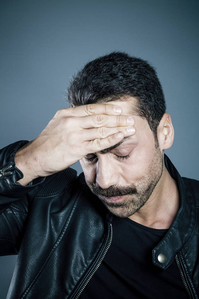 Young handsome man with beard and mustache suffering from headache studio shot against blue background - Φωτογραφία, εικόνα