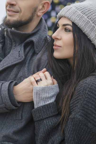 Linda mulher caucasiana bonita com um homem em um passeio na cidade europeia no inverno. Casal usar roupa cinza casual e abraçando uns aos outros. Tempo frio, luzes de Natal em um fundo
 - Foto, Imagem