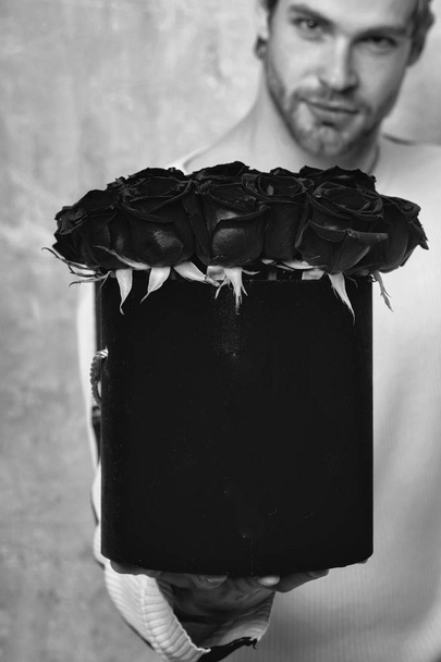 bearded man holds red rose box on textured wall - Foto, afbeelding