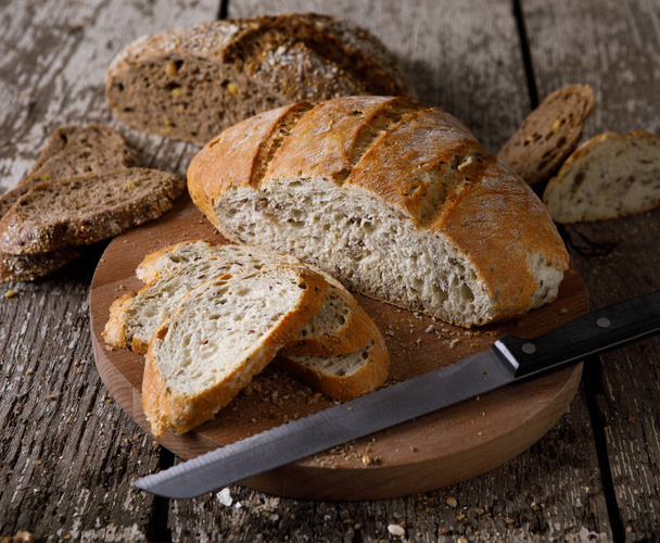 Fresh bread slice and cutting knife on rustic table. - Photo, Image