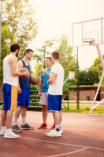 Cuatro jugadores de baloncesto tienen trato antes del partido. Están de pie en la cancha y hablando con sonrisa en su cara.
. - Foto, imagen