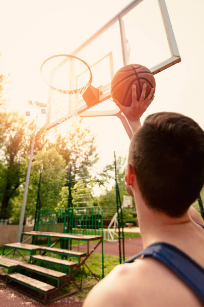 Young man training basketball on street court. He throw ball to hoop. Rear view. - Foto, Imagem