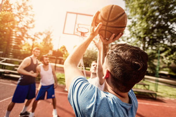 Four basketball players have a training outdoor. Selective focus. Focus on foreground, on rear view man shooting free throw. - Photo, Image