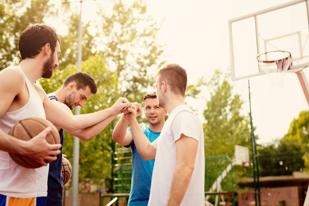 Cuatro jugadores de baloncesto que tienen un saludo deportivo antes del entrenamiento. Son golpes de puño con sonrisa en la cara
. - Foto, Imagen