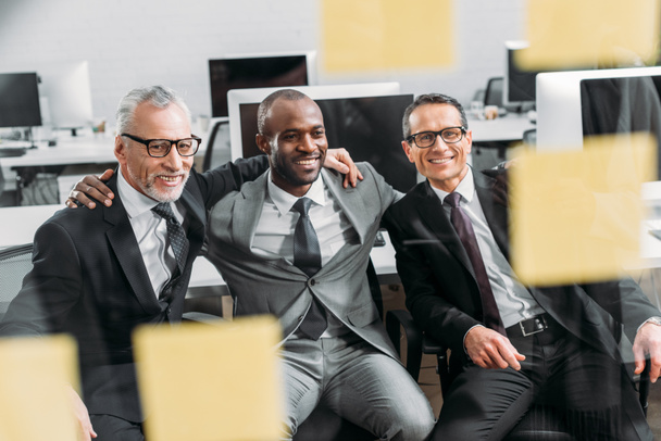uomini d'affari multiculturali sorridenti che guardano gli appunti durante la riunione in ufficio
  - Foto, immagini