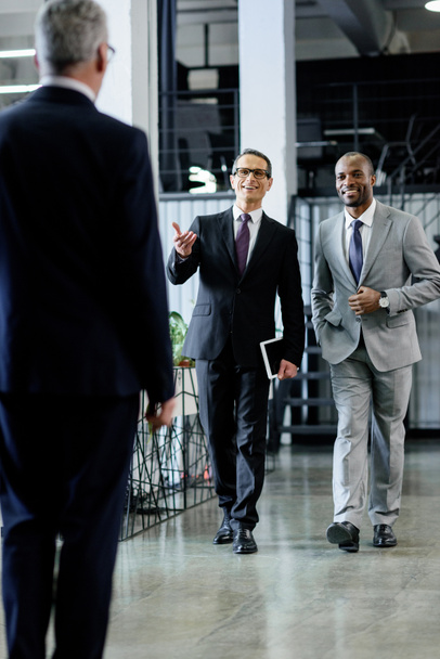 empresários sorridentes multiétnicos em ternos andando no escritório
 - Foto, Imagem
