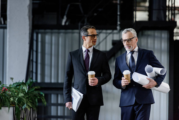 portrait of businessmen with coffee to go in hands walking in office - Photo, Image