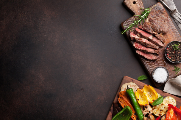 Légumes grillés et steak de boeuf sur planche à découper sur table en bois. Vue supérieure avec espace de copie
 - Photo, image