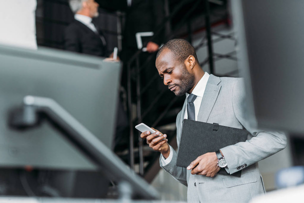 Selektywny fokus z Afryki amerykański biznesmen z dokumentów przy użyciu smartfona - Zdjęcie, obraz