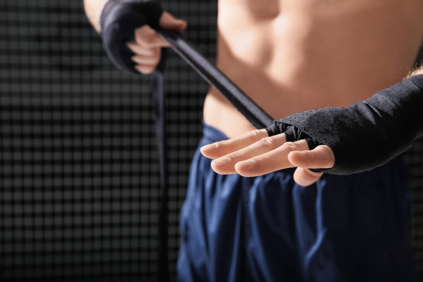 Young boxer applying wrist wraps in gym, closeup - Фото, зображення