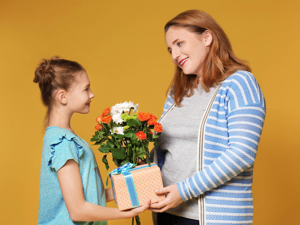 Cute little girl giving her mother present and flowers on color background - Valokuva, kuva
