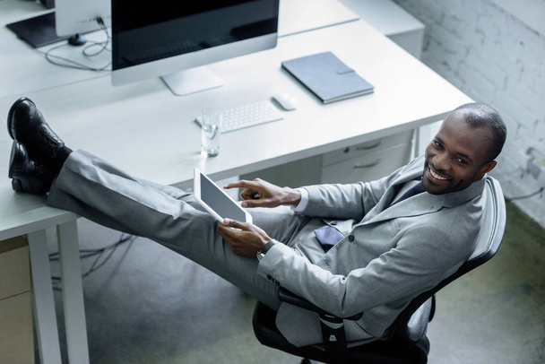 hymyilevä afrikkalainen amerikkalainen liikemies, jolla on tabletti työpaikalla
 - Valokuva, kuva