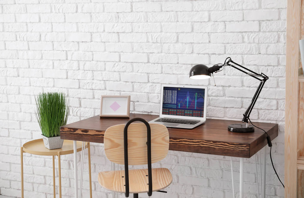 Comfortable home workplace with laptop on desk against brick wall - Фото, изображение
