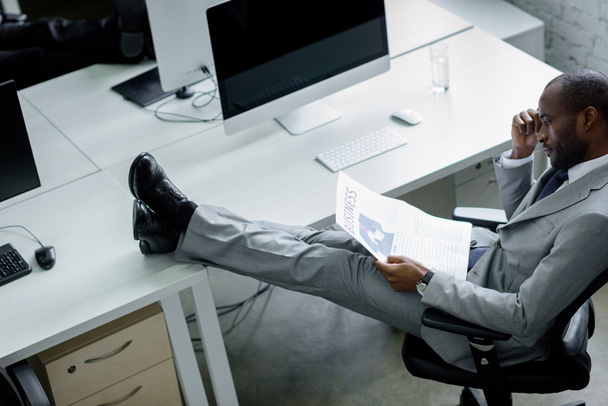 african american businessman reading newspaper at workplace - Fotó, kép