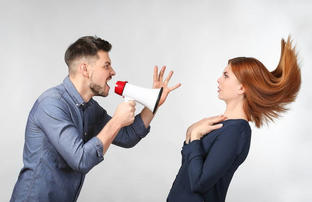 Angry man with megaphone scolding his wife on light background - Fotó, kép