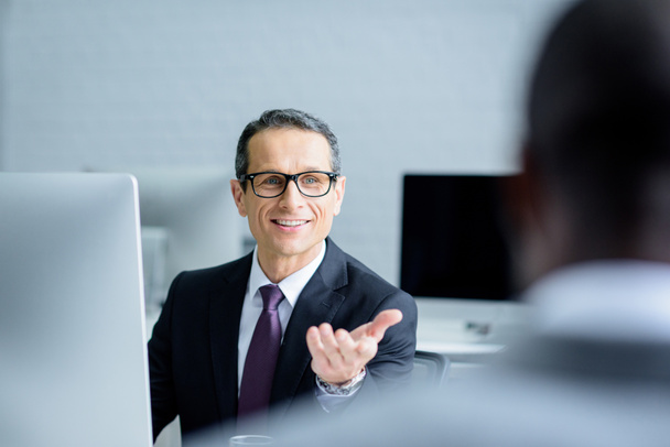 enfoque selectivo de sonriente hombre de negocios hablando con su colega mientras trabaja en la oficina
 - Foto, Imagen