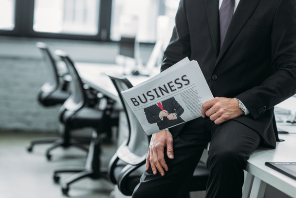 partial view of businessman with newspaper sitting on table in office - Foto, afbeelding