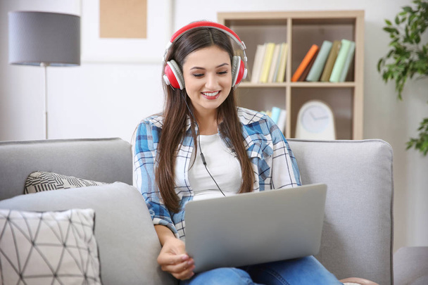 Woman listening to audiobook through headphones at home - Fotó, kép