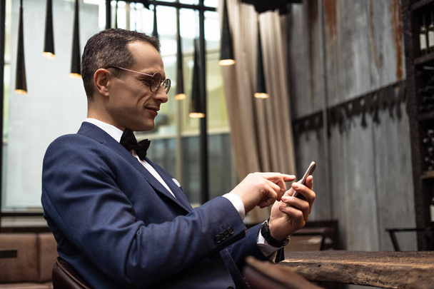 handsome man in stylish suit using smartphone at restaurant - Фото, зображення